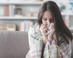 Sick young woman at home on the sofa with a cold, she is covering with a blanket and blowing her nose